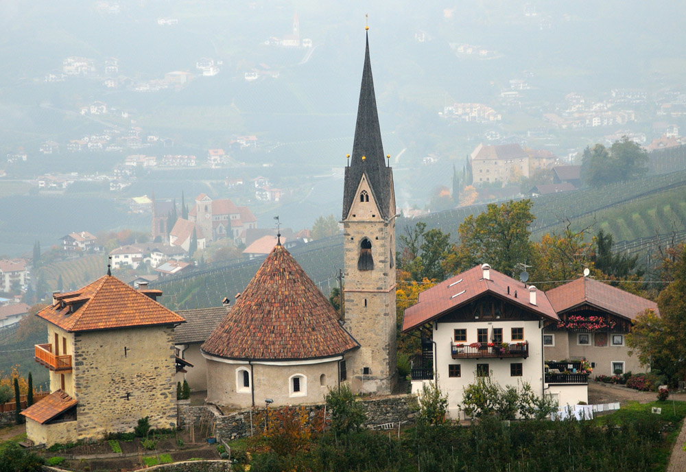 ...Die Kirche liegt im Weiler St. Georg in 716 m s.l.m. im Oberdorf von Schenna (600 m). Sie befindet sich neben der ursprünglichen Ministerialenburg der Herren von Schenna, von der nur das Fundament des Bergfrieds erhalten ist. Auf ihm wurde ein Wohnhaus, der Uhlenturm, errichtet. In unmittelbarer Nachbarschaft liegen zwei Höfe, die gastronomisch genutzt werden...